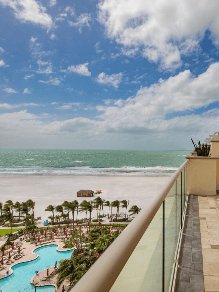 Relaxing beach view from a hotel balcony overlooking the ocean, pool, and sandy shoreline.