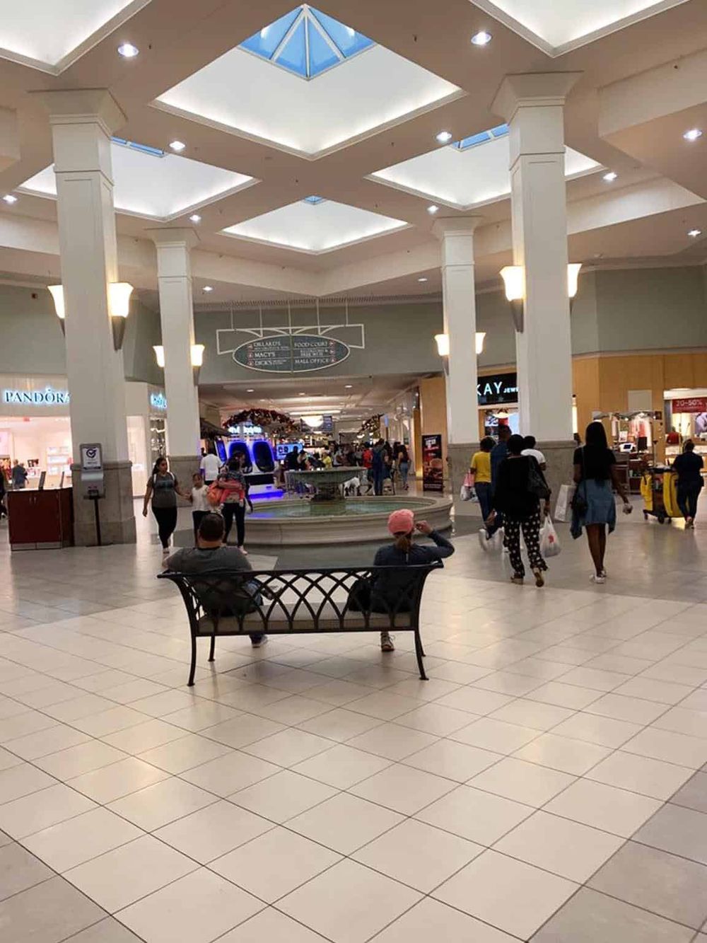 Bright indoor shopping mall with benches and shoppers, offering directions and mall services.