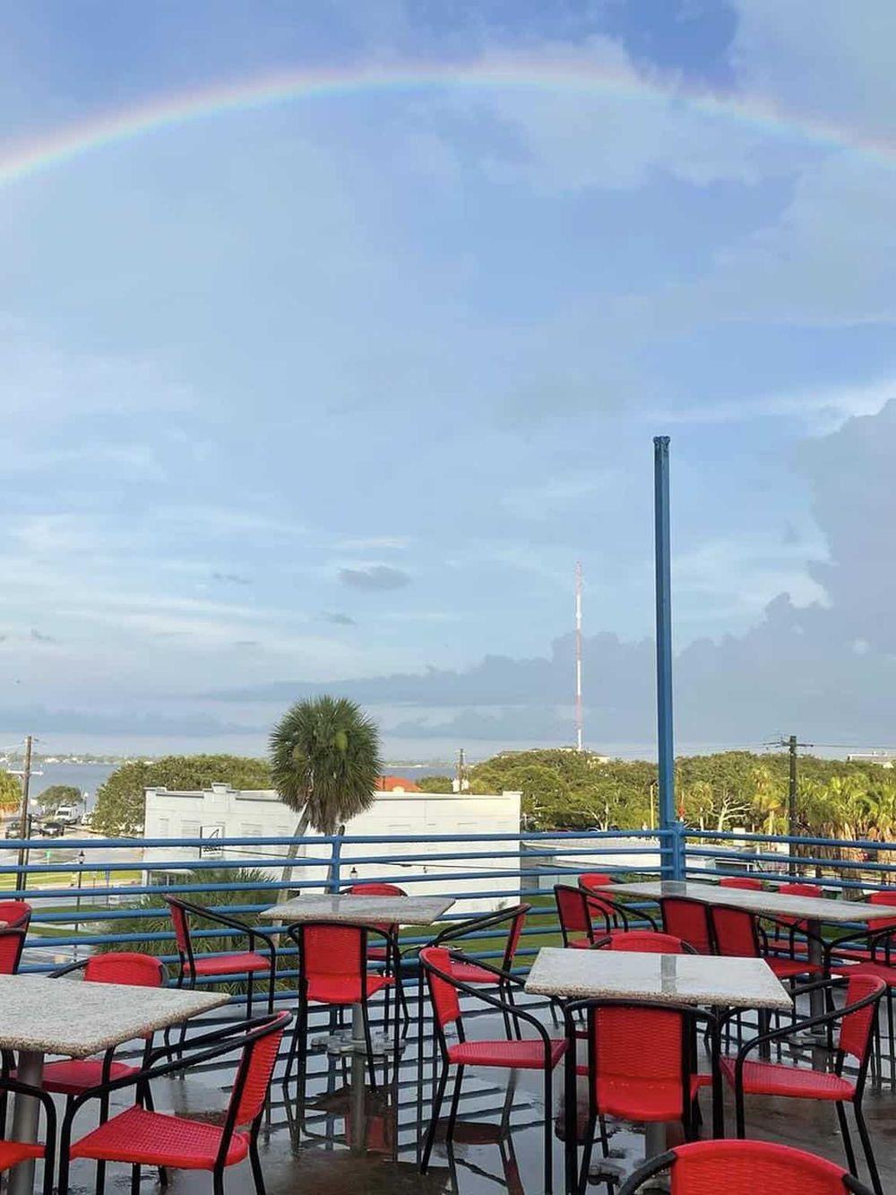 Colorful outdoor restaurant seating with a rainbow in the sky, scenic views, and tropical landscape.