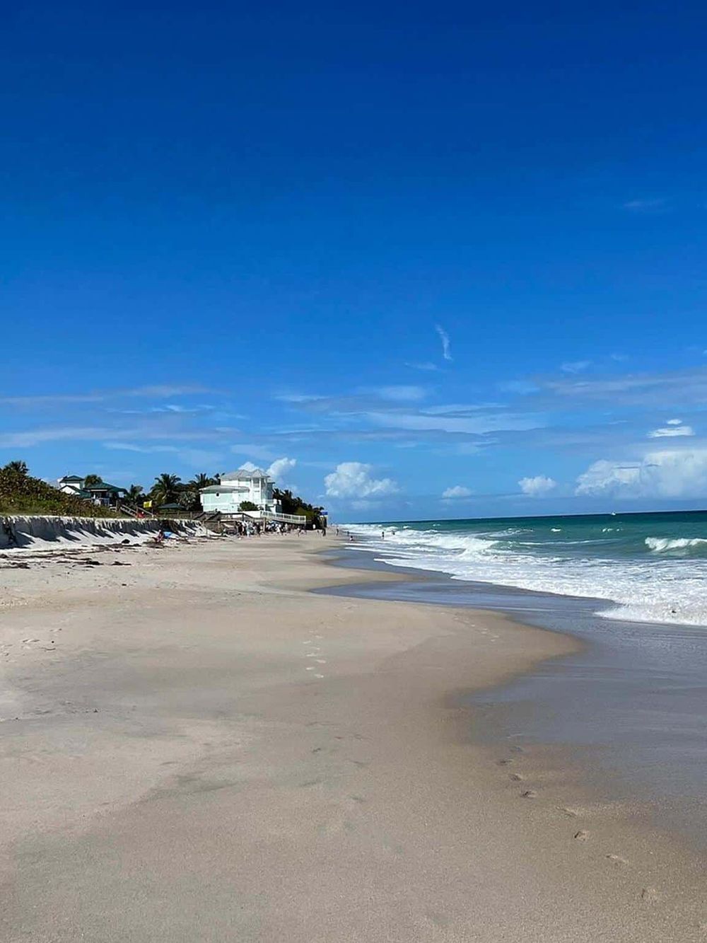 Bright sunny beach with clear blue sky, sandy shoreline, ocean waves, and beachfront houses for perfect seaside relaxation.
