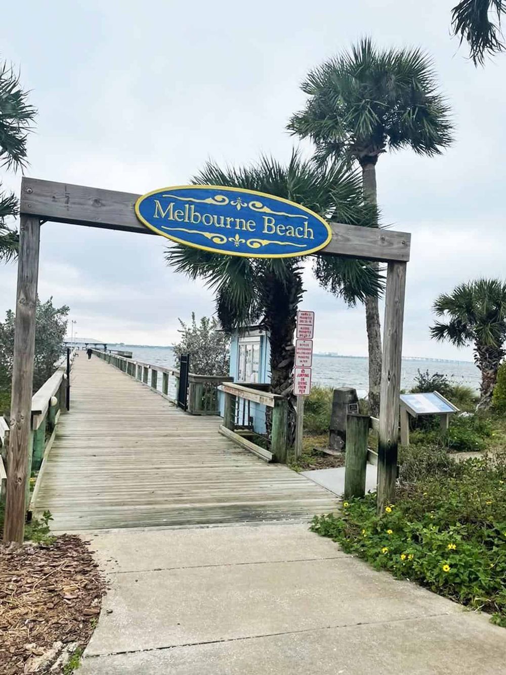 Scenic view of Melbourne Beach pier with wooden walkway and tropical palm trees, perfect for beachside relaxation.