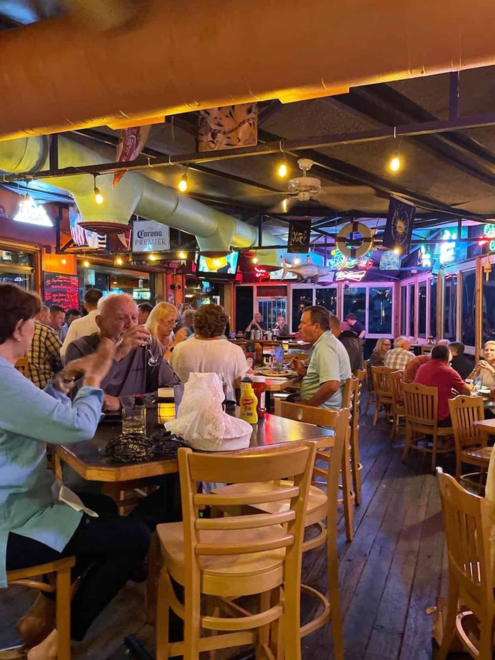 Cozy restaurant interior with colorful neon signs, diverse diners, and nautical decor, ideal for a casual night out.