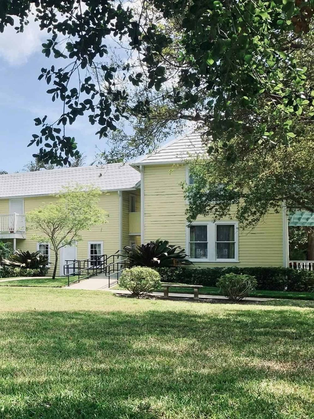 Beautiful yellow residential building with green lawn and trees, accessible entryway and peaceful outdoor environment.