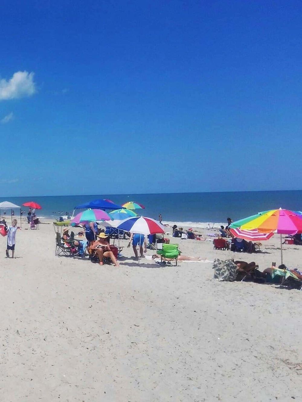 Colorful beach umbrellas and people enjoying a sunny day at the ocean shoreline.
