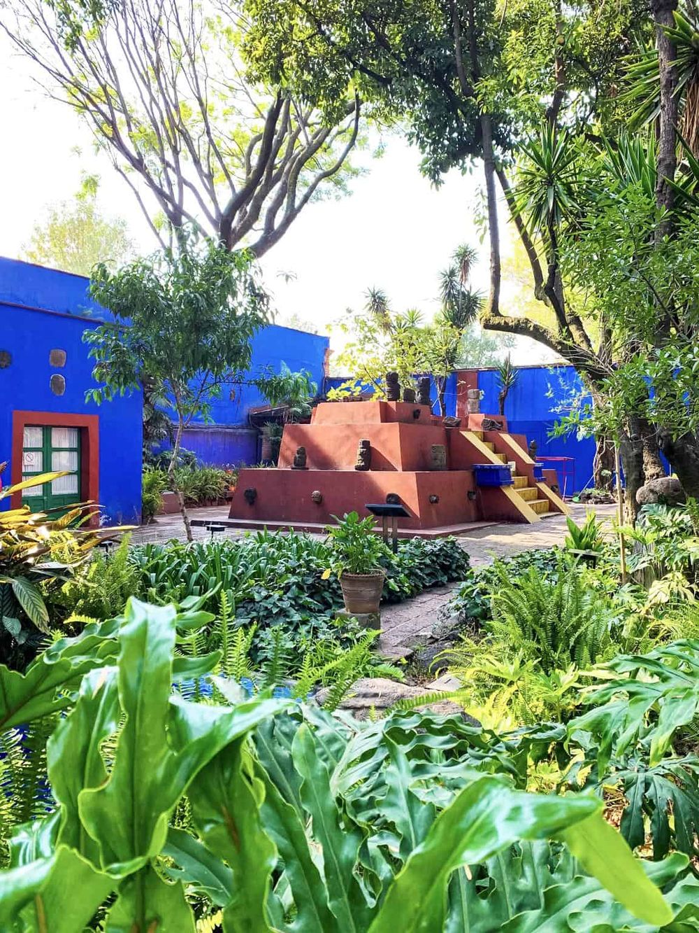 Lush green garden with vibrant blue walls, colorful stairs, and tropical plants, enhancing outdoor relaxation and beauty.