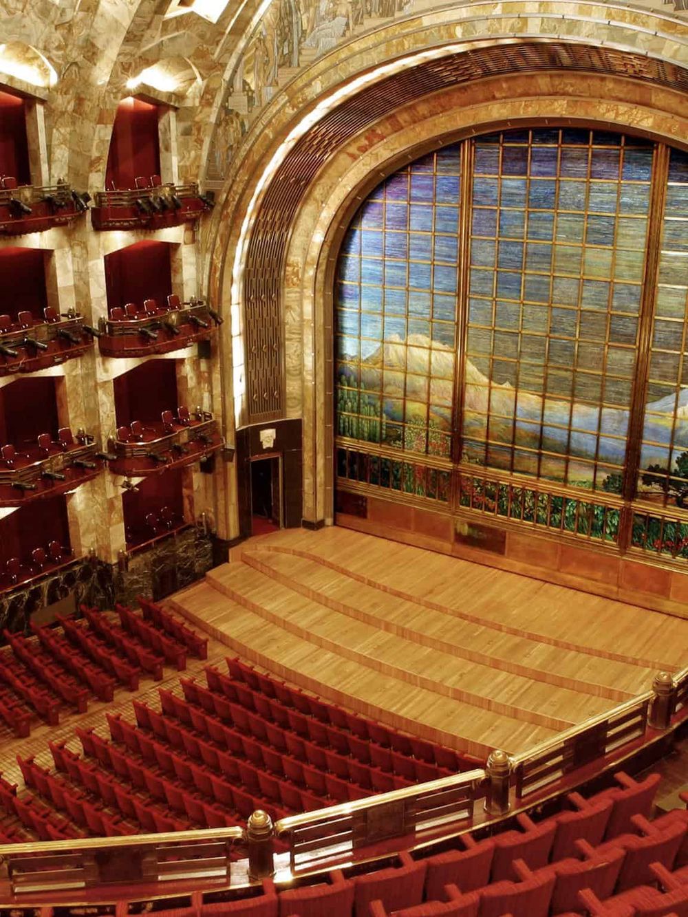 Impressive theater stage with a beautiful mountain landscape stained glass backdrop. Luxurious interior with red seats and elegant design.