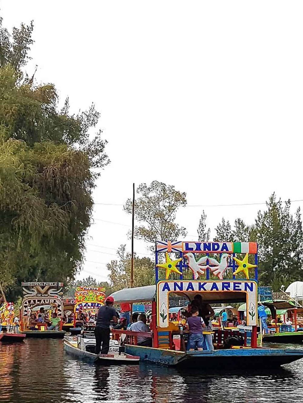 Colorful traditional Mexican boat floating on calm water with lush trees in background.