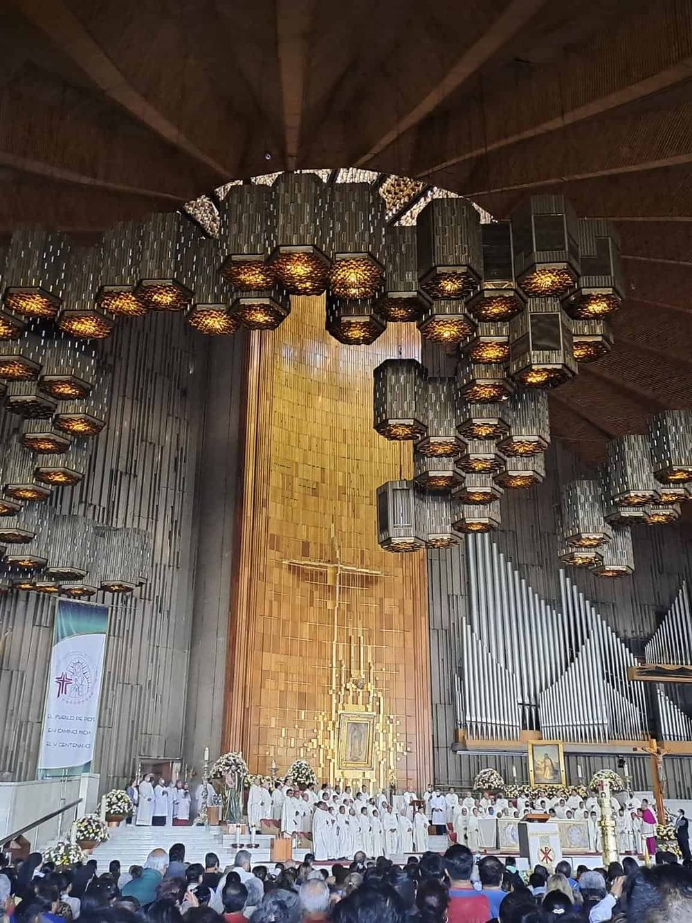 Bright church interior with hanging lanterns and a large congregation during a religious ceremony.