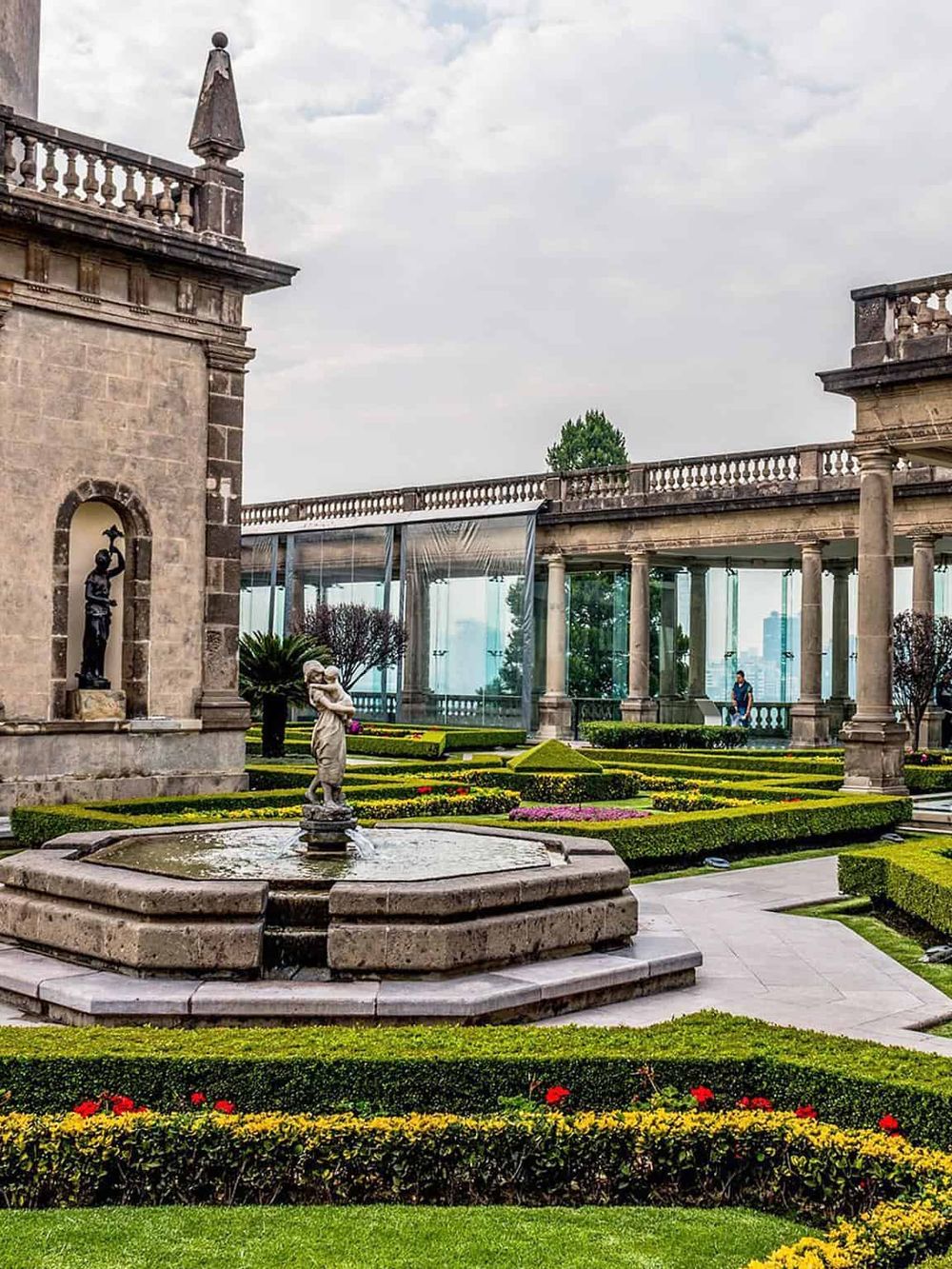 Charming historic garden with fountains, sculptures, and classical architecture surrounded by lush greenery.