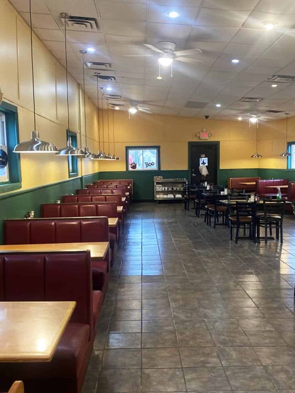 Cozy restaurant interior with red booths, black tables, yellow and green walls, modern lighting, and tiled flooring.