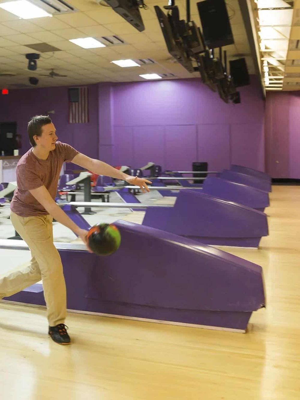 Bowling alley with purple lanes and a young man rolling a bowling ball at QuestForDirections.