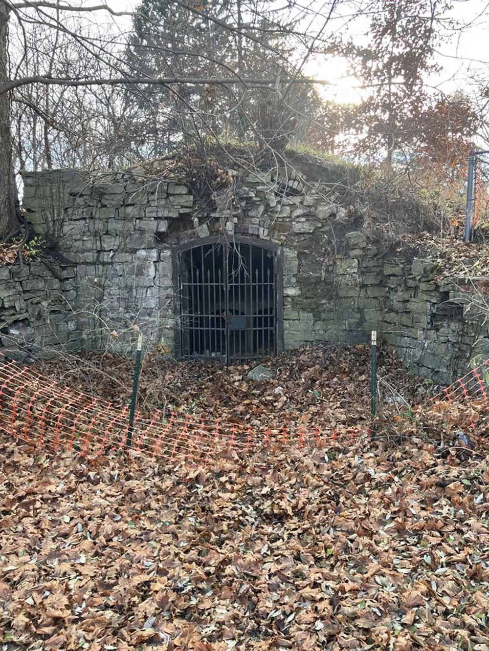 Hidden underground tunnel entrance with stone archway, surrounded by fallen autumn leaves and fencing.