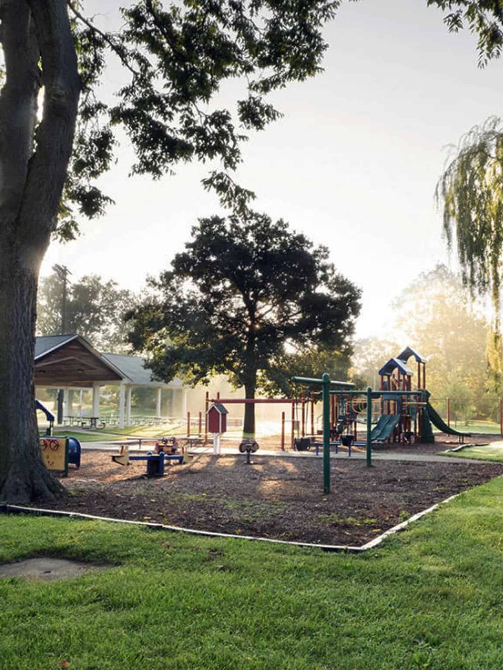 Bright playground scene in a park with trees, slides, swings, and walking paths, perfect for family activities and outdoor fun.