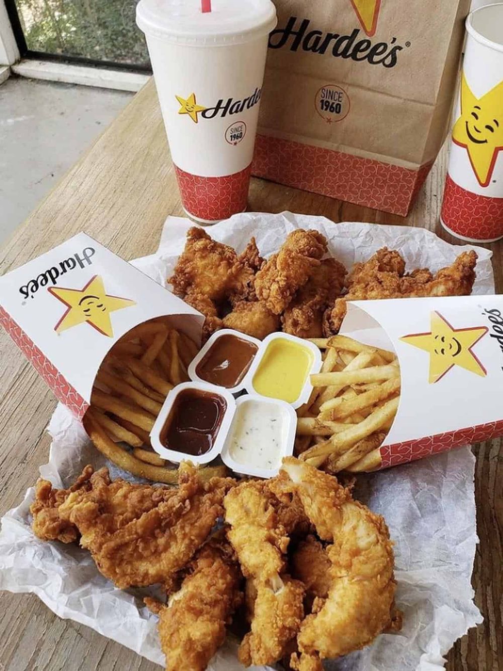 Crispy fried chicken with French fries, dipping sauces, and soft drinks at Hardee's.