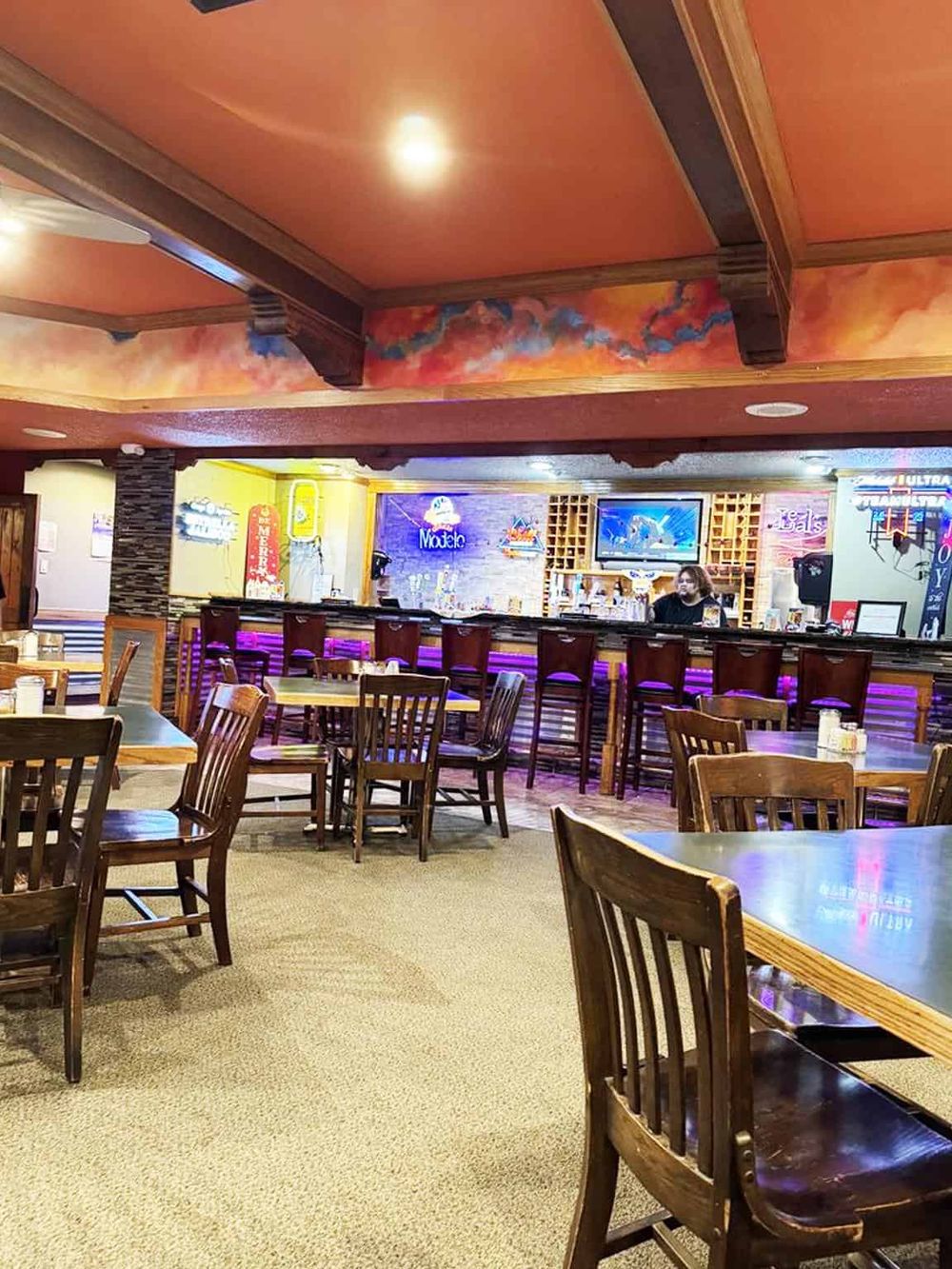 Vibrant bar and restaurant interior with wooden furniture, colorful ceiling art, and neon signs, perfect for dining and socializing.