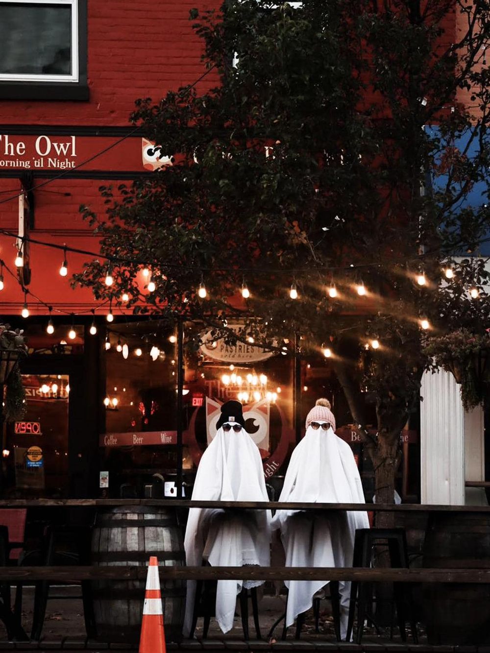 Ghosts dressed in white costumes with sunglasses at a cozy outdoor bar, perfect for nightlife adventures.