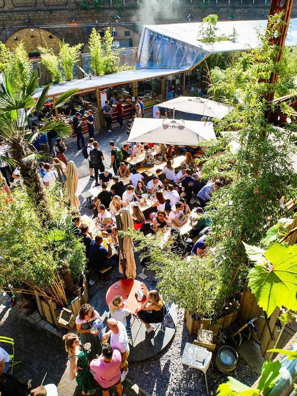 Vibrant outdoor dining area at QuestForDirections restaurant, with lush greenery and lively crowd enjoying meals.