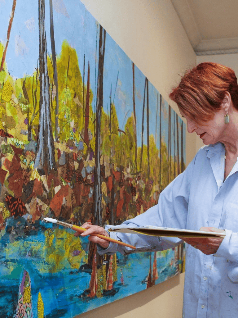 Vibrant woman painting colorful forest scene on large canvas at art gallery.