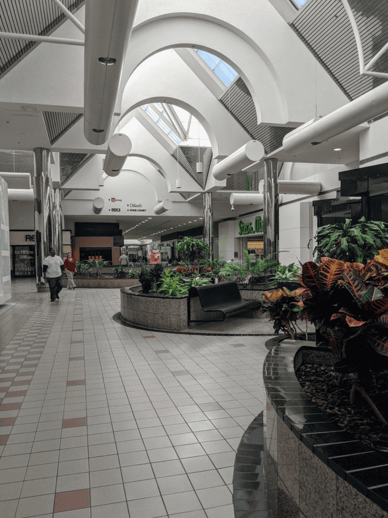 Indoor shopping mall with modern architecture, greenery, and seating areas.