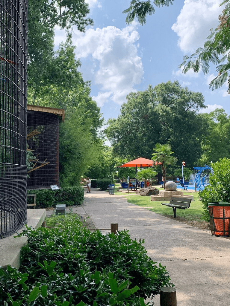 Lush green park with playground, shade umbrellas, and walking path, perfect for family fun and outdoor activities.