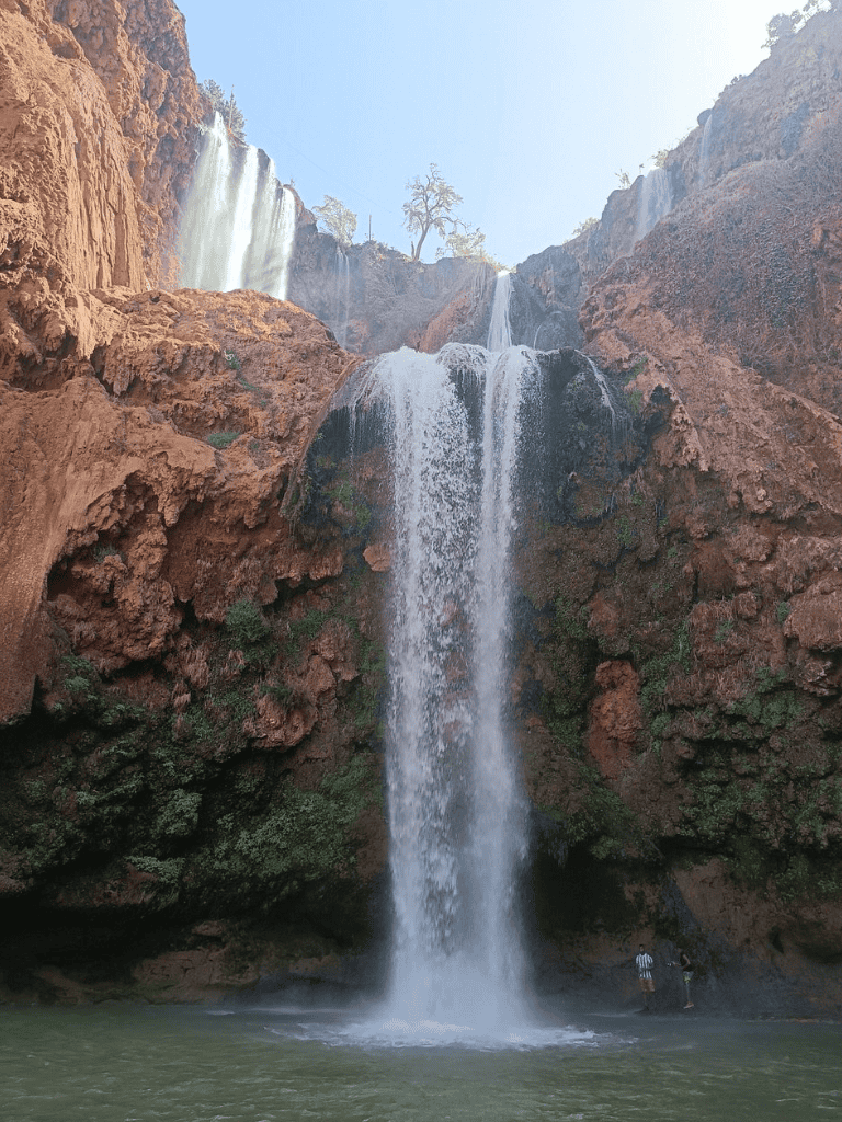 Vivid waterfall cascading down red rocky cliffs with lush greenery, outdoor adventure, scenic natural beauty, travel destination.