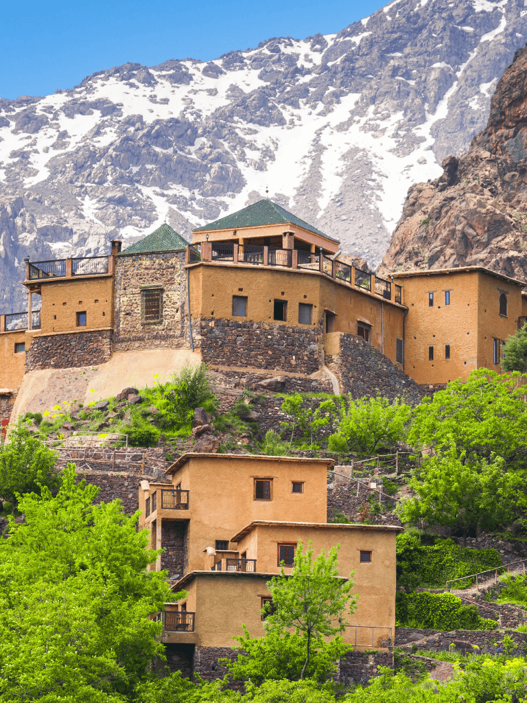 Colorful mountain resort nestled on rocky terrain with lush greenery and snow-capped peaks in the background.