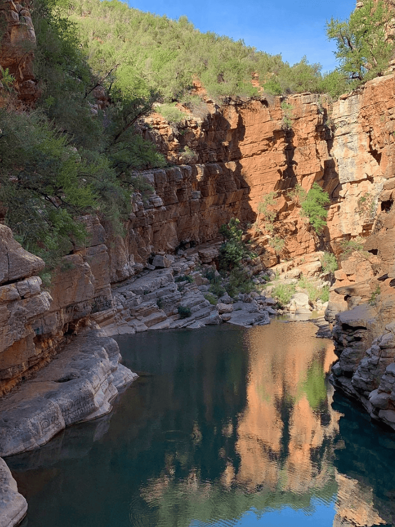 Serene canyon with red rock cliffs and reflective water at Quest for Directions.