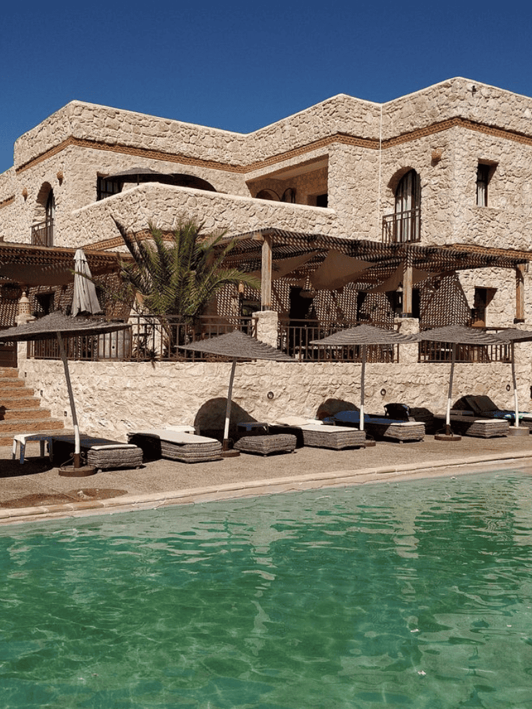 Luxurious desert resort with stone architecture, poolside loungers, and shaded umbrellas for relaxation.