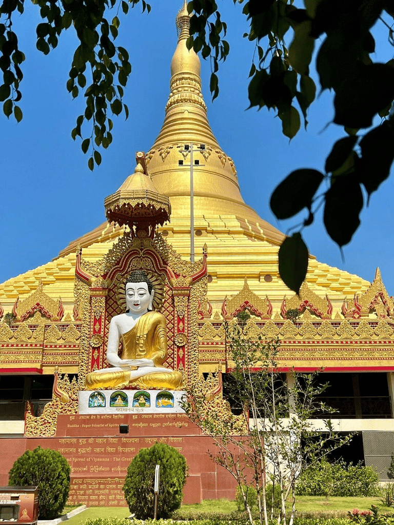 Golden Buddhist stupa with reclining Buddha statue, vibrant temple architecture, lush greenery, clear blue sky, spiritual and cultural landmark.