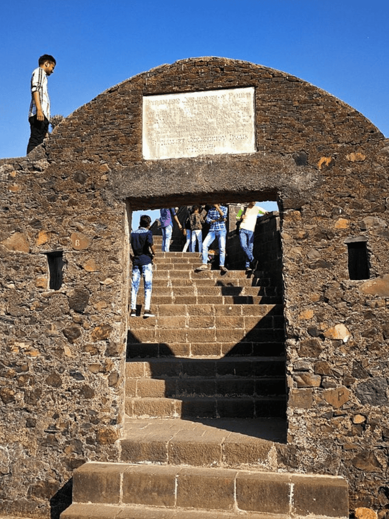 Ancient stone archway with tourists climbing steps at a historical site.