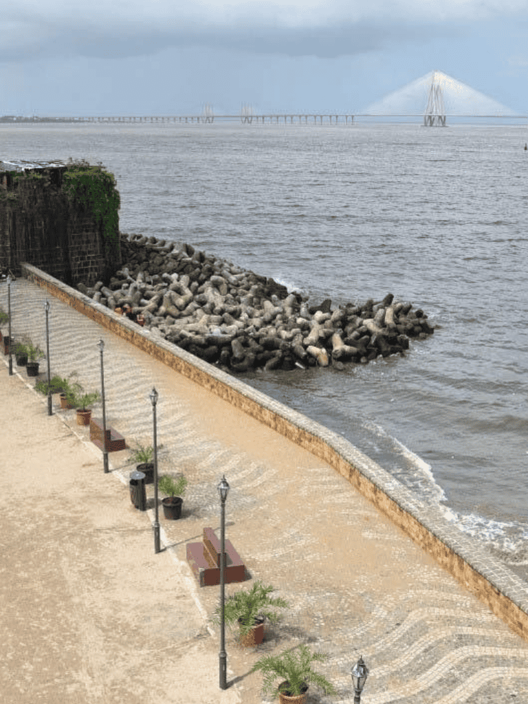 Scenic seaside promenade with lampposts and planters, overlooking a bridge and ocean.