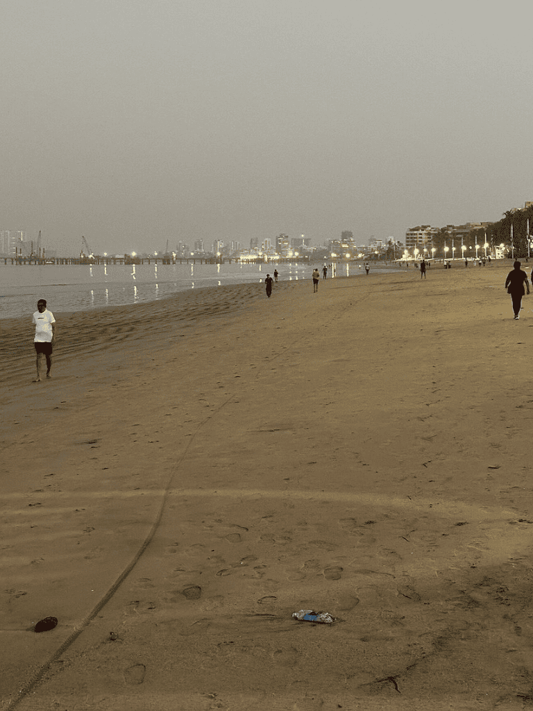 Empty beach with city skyline, evening lights, and calm waters, ideal for relaxation and sunset views.