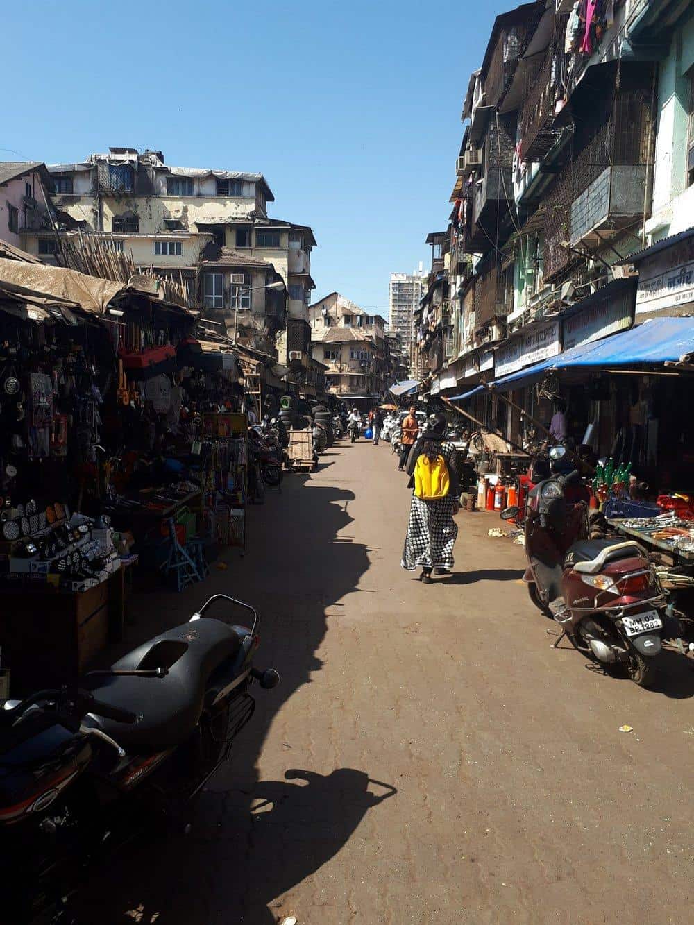 Colorful street market in Mumbai with shops, stalls, and scooters on a sunny day.