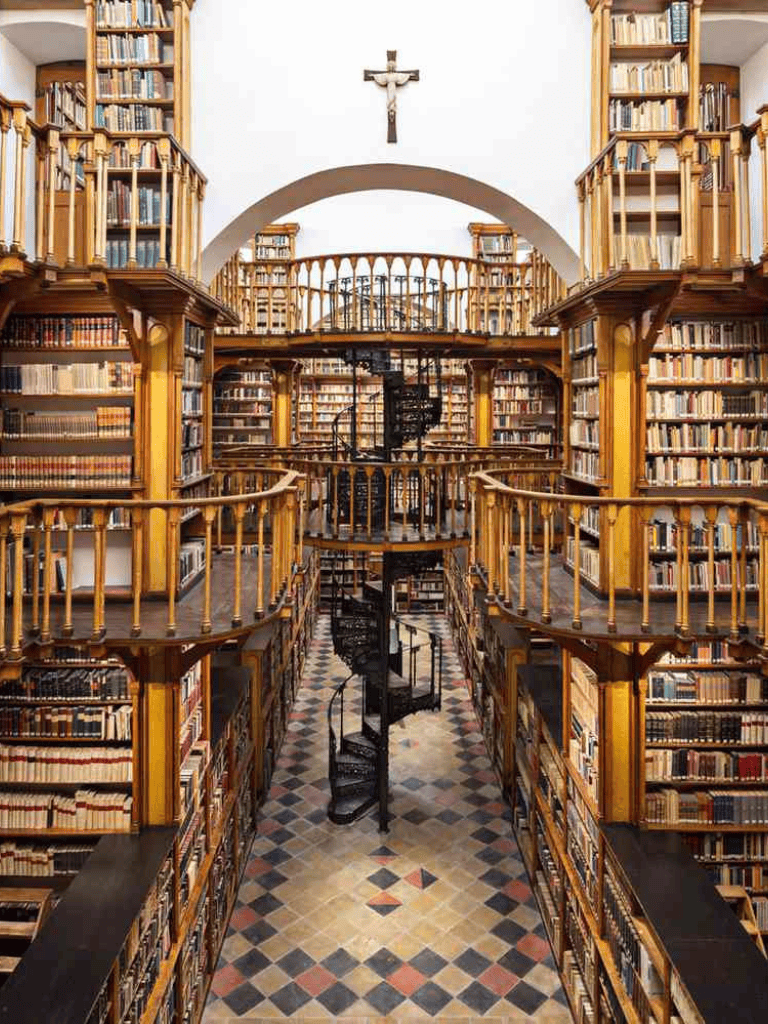 Intricate wooden bookcase in grand historic library with spiral staircase and crucifix on the wall.