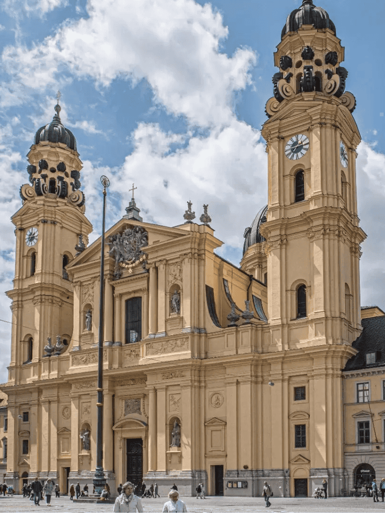 Impressive Baroque church with twin towers and intricate architecture in a bustling city square.