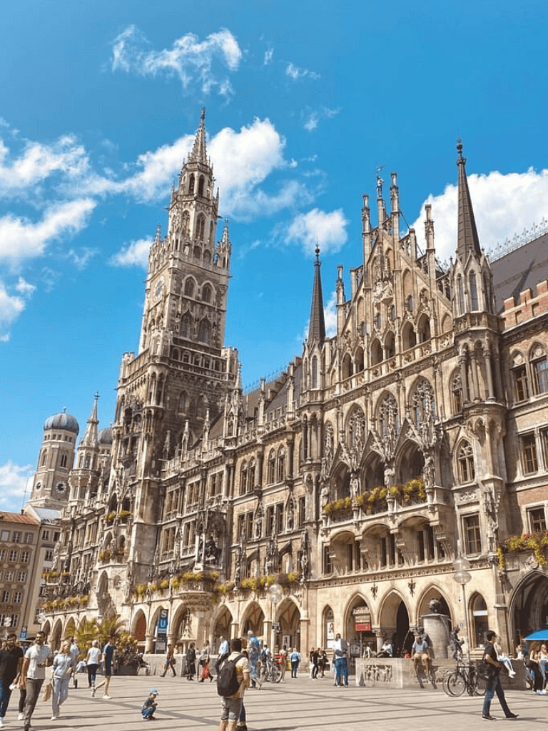 Historic Gothic architecture at Marienplatz in Munich, Germany, with bustling crowd and clear blue sky.