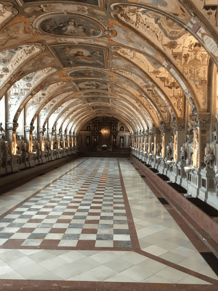 Ornate Vatican Museum hallway with detailed ceiling, sculptures, and checkerboard floor.