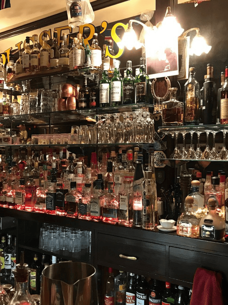 Assorted liquor bottles and bar glasses at a colorful bar setting.