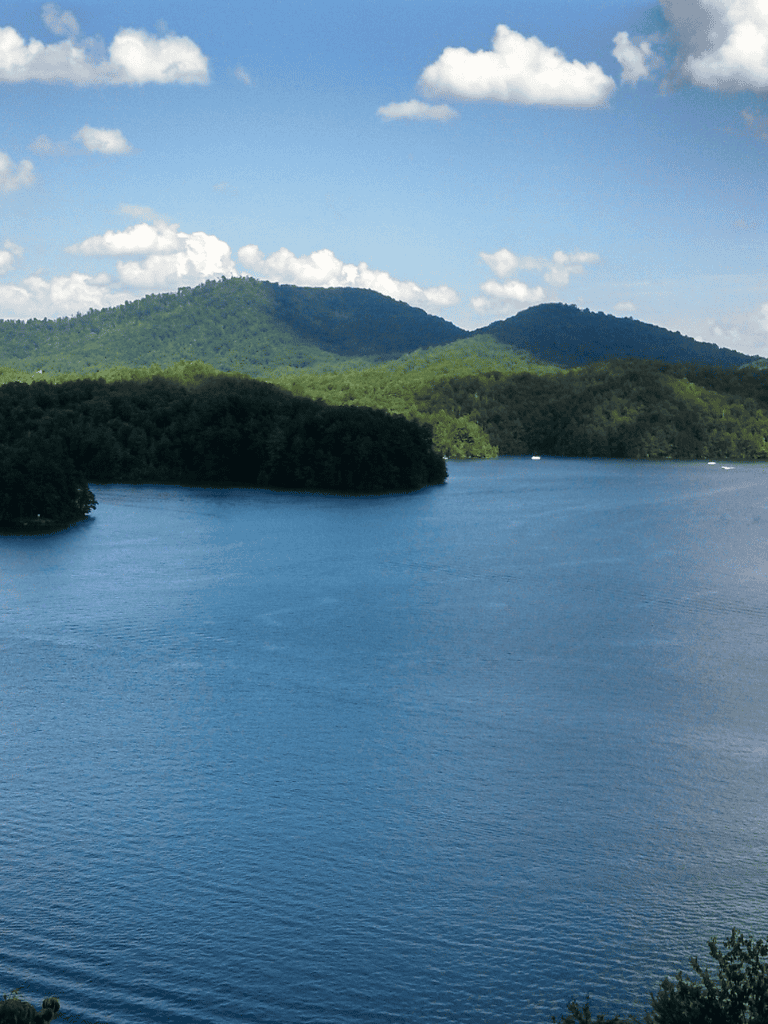 Serene lake with lush green mountains and blue sky, perfect for nature and outdoor exploration.