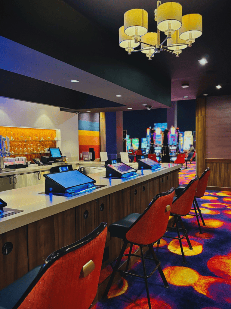 Computerized casino gaming machines inside a vibrant casino with colorful carpet and ambient lighting.