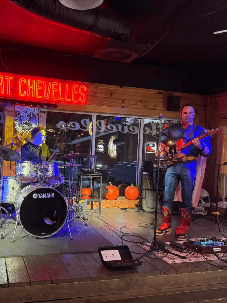 Live music performance at QuestForDirections venue with colorful lighting and Halloween decorations.