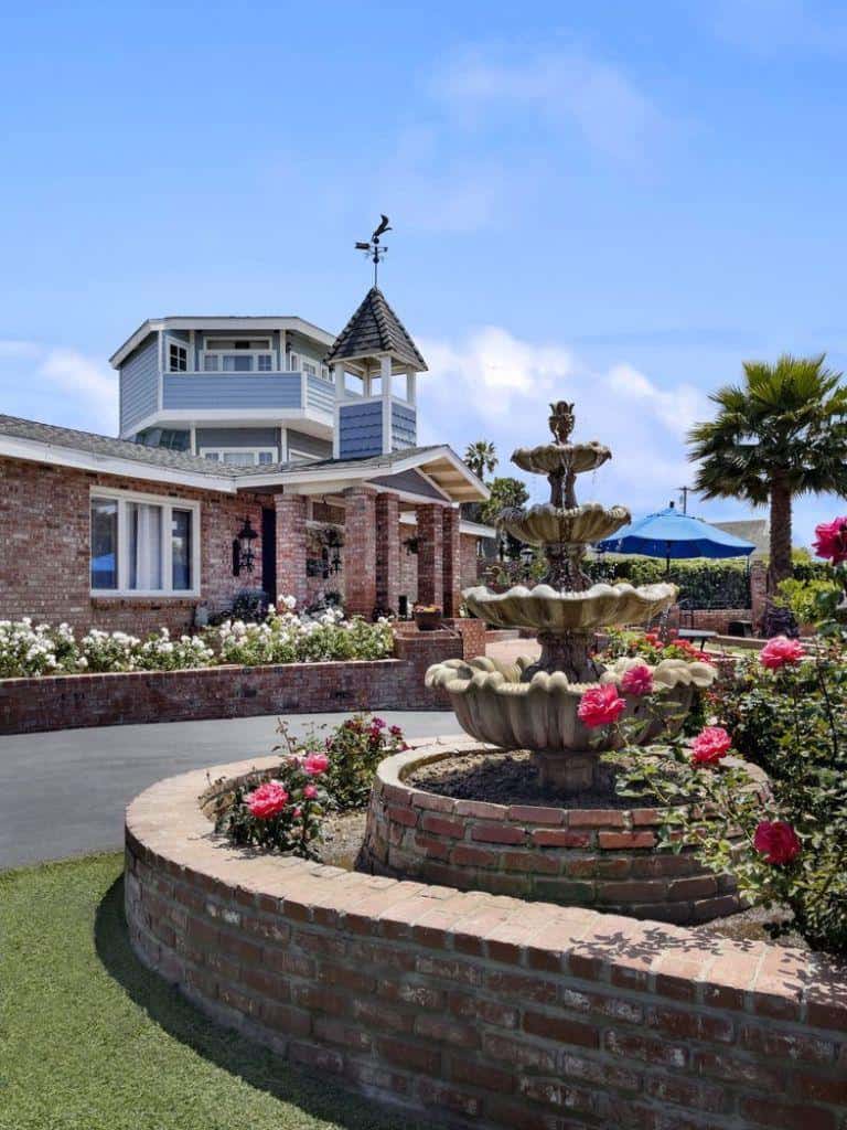 Charming brick house with decorative fountain and vibrant garden in warm outdoor setting.