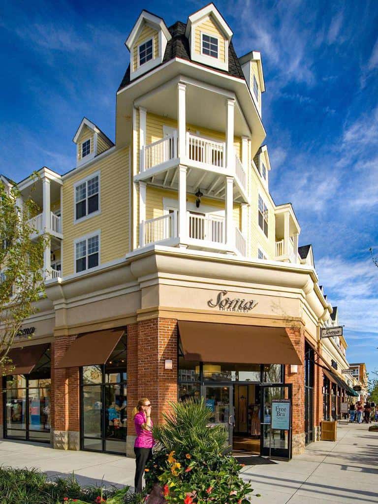 Charming yellow apartment building with retail shops and outdoor cafes, vibrant shopping district in daylight.