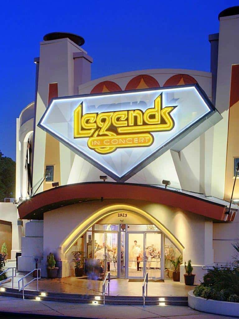 Huge neon "Legends in Concert" sign above theater entrance, modern building exterior at dusk.