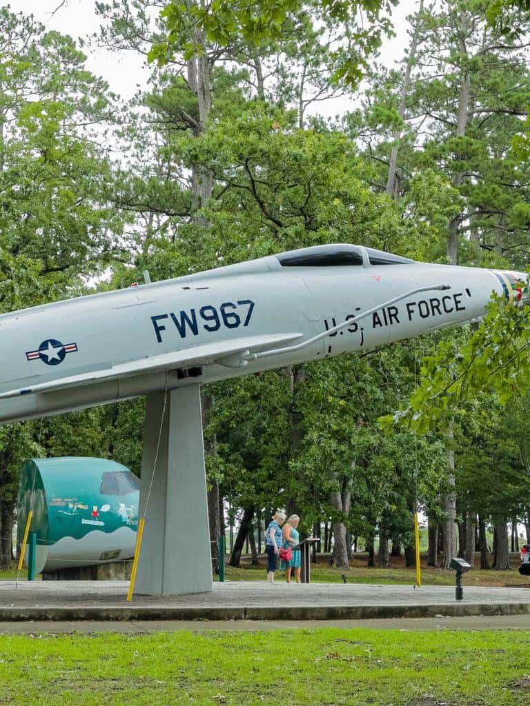 U.S. Air Force jet monument at QuestForDirections outdoor exhibit with visitors, forest background.