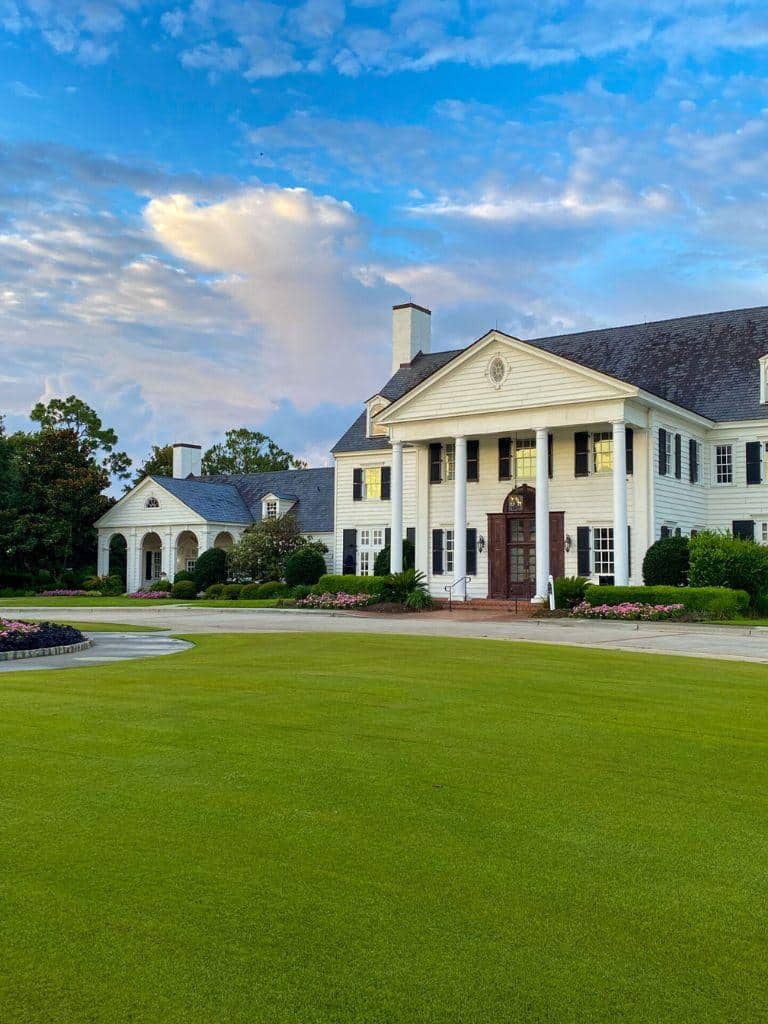 Elegant white southern mansion with lush green lawn and landscaping, sunny sky and classic architecture.