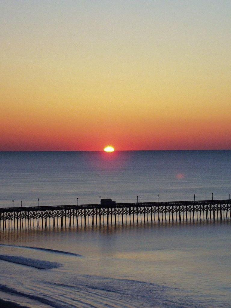 Stunning sunset over the ocean with a pier at dusk, perfect for seaside travel and relaxation.
