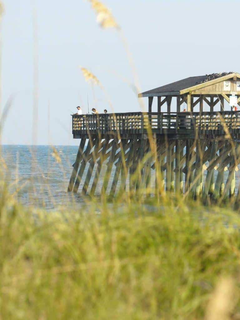 Seaside wooden pier with people enjoying the ocean view and sunshine.