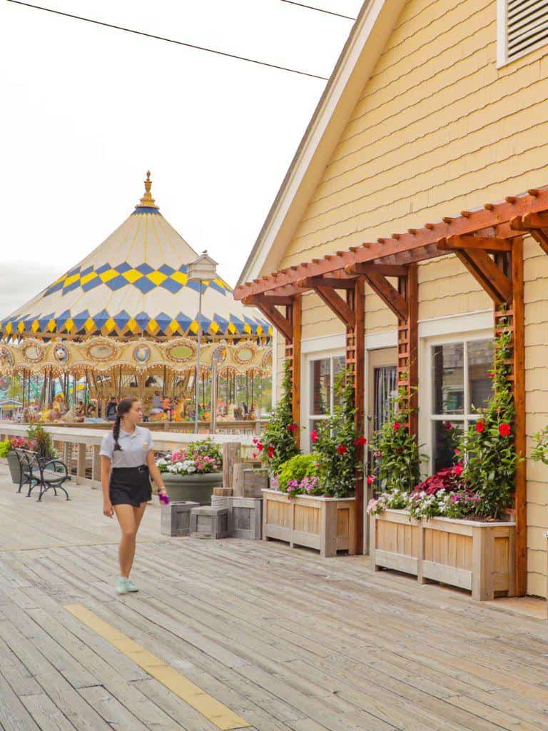 Colorful carousel near a yellow building with flower planters and wooden deck, bright amusement park scene.