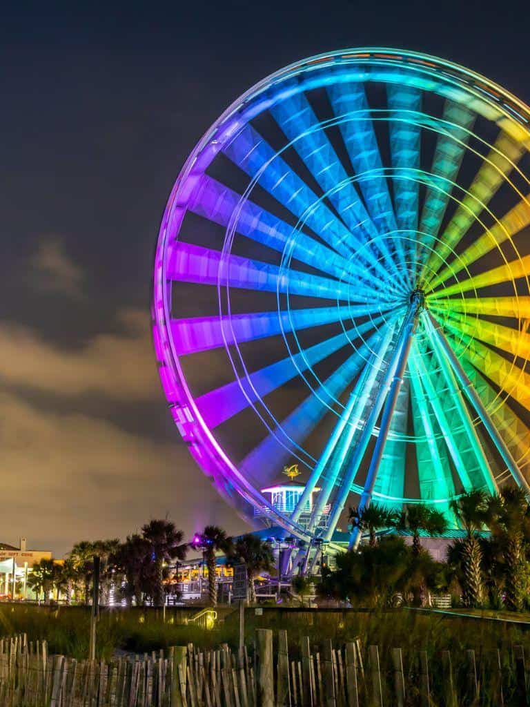 Colorful illuminated Ferris wheel spinning at night for attractions and entertainment.